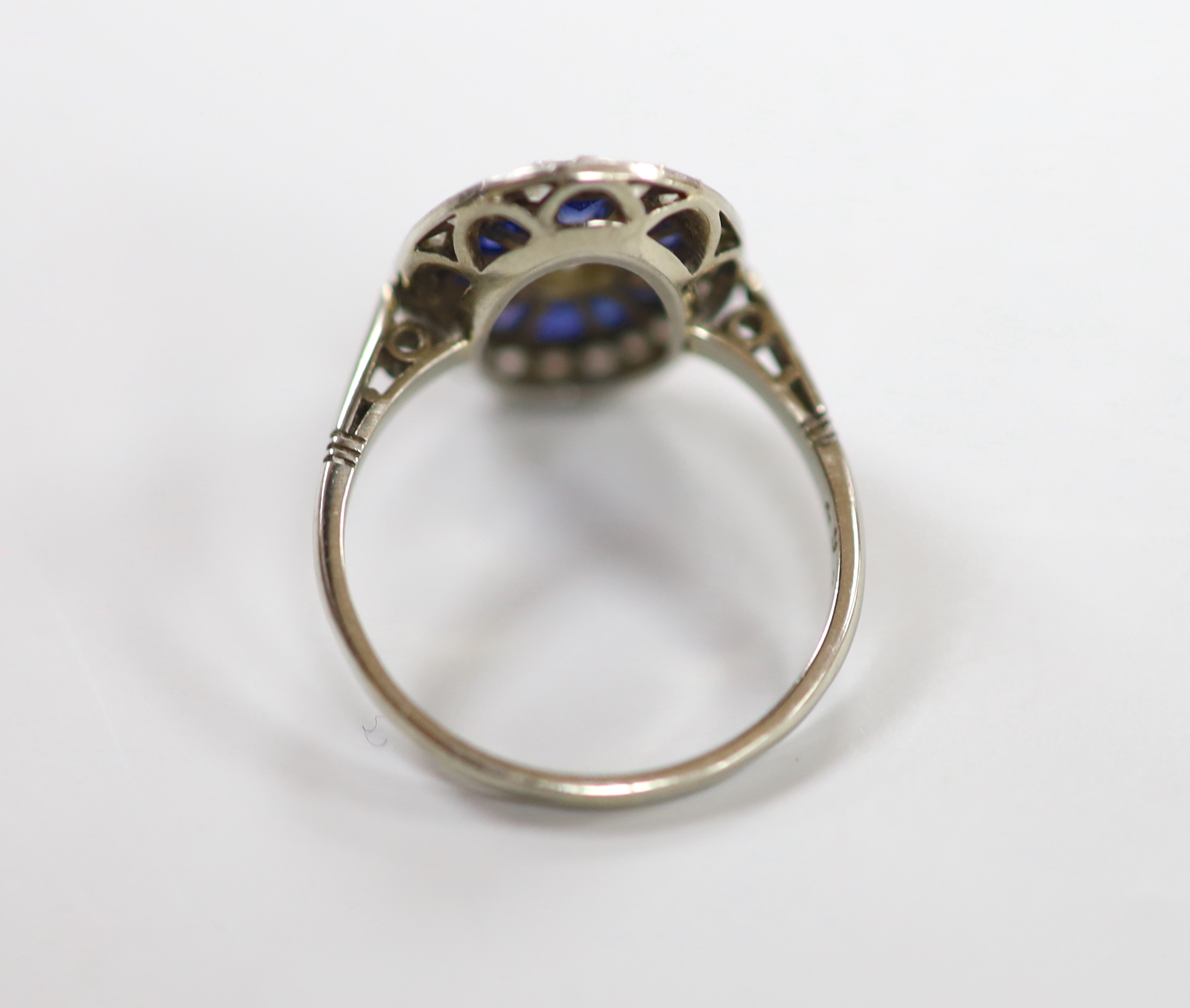 A 1920's white metal, sapphire and diamond oval cluster ring, set with round cut diamonds and shaped cut sapphires, size M/N, gross weight 3.3 grams.